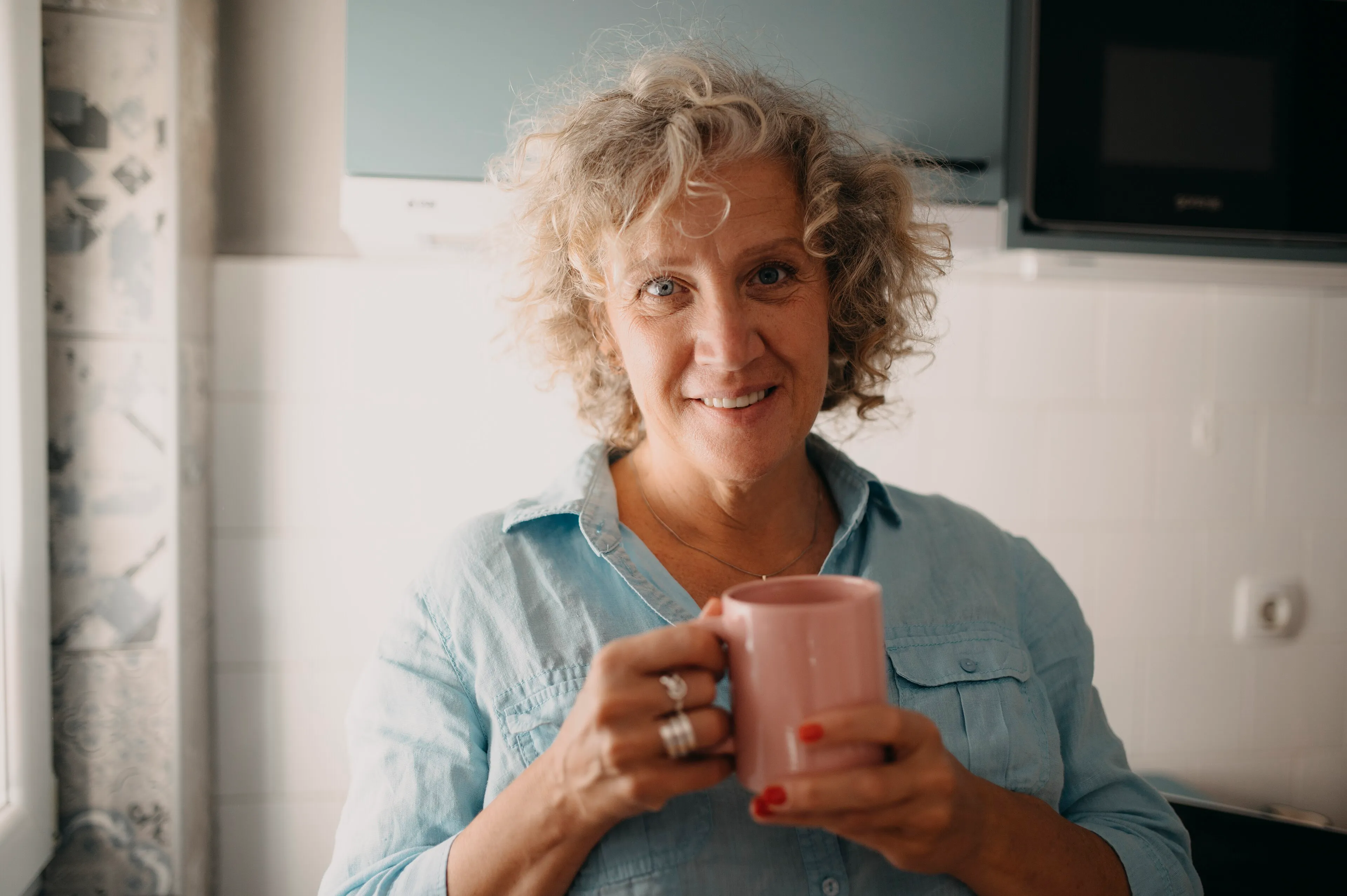 Mujer de mediana edad sonriente con una taza en la cocina de su casa